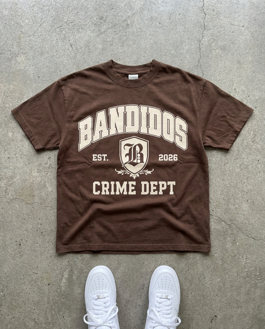 BANDIDOS CRIME DEPT TEE laid flat on concrete – brown tee with cream BANDIDOS CRIME DEPT varsity graphic