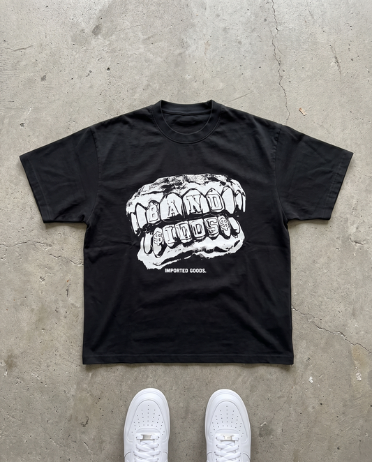 BANDIDOS GRILL TEE laid flat on concrete – black tee with white BANDIDOS grillz graphic and IMPORTED GOODS text