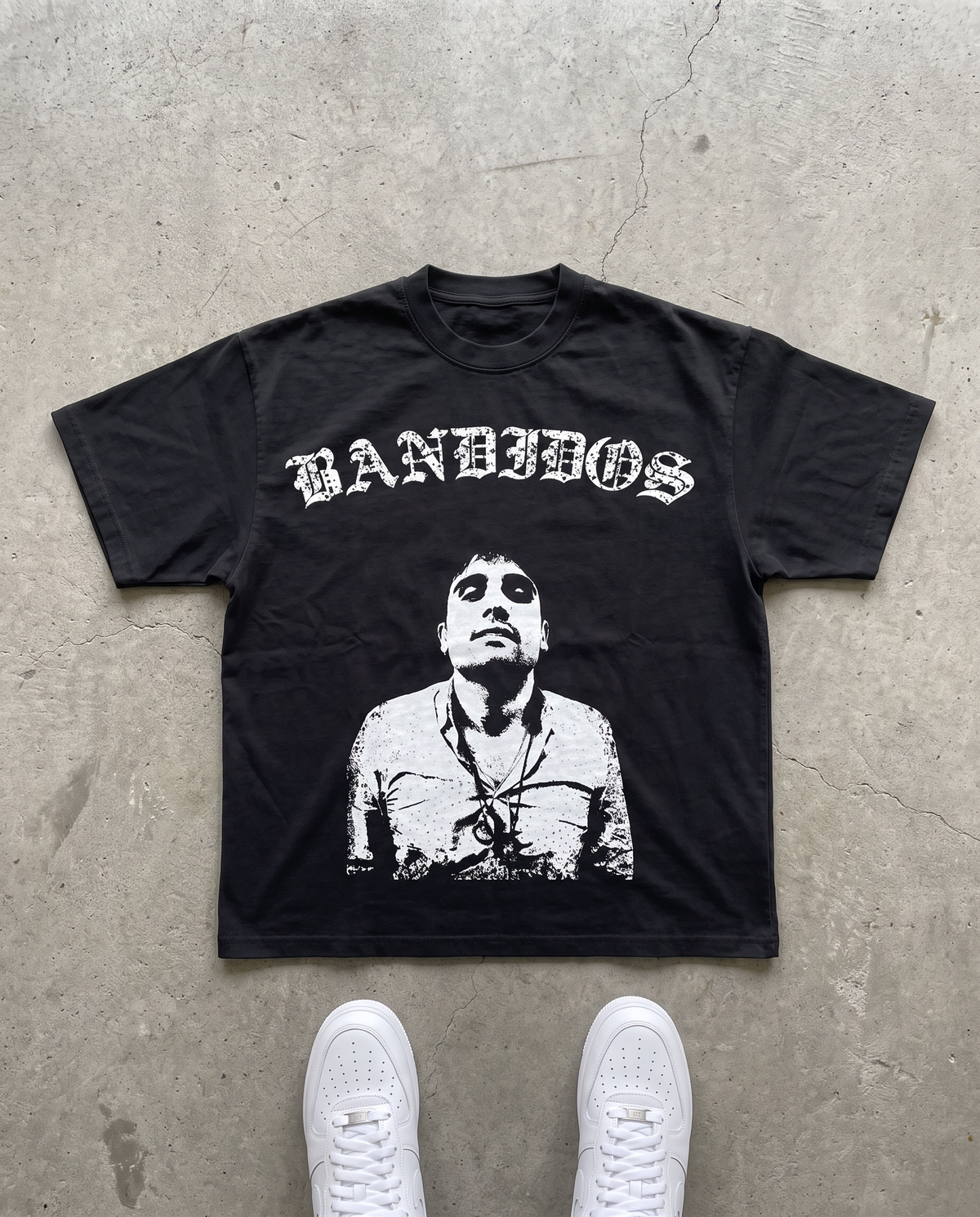 BANDIDOS OVIDIO GUZMAN TEE laid flat on concrete – black tee with white BANDIDOS logo and portrait graphic